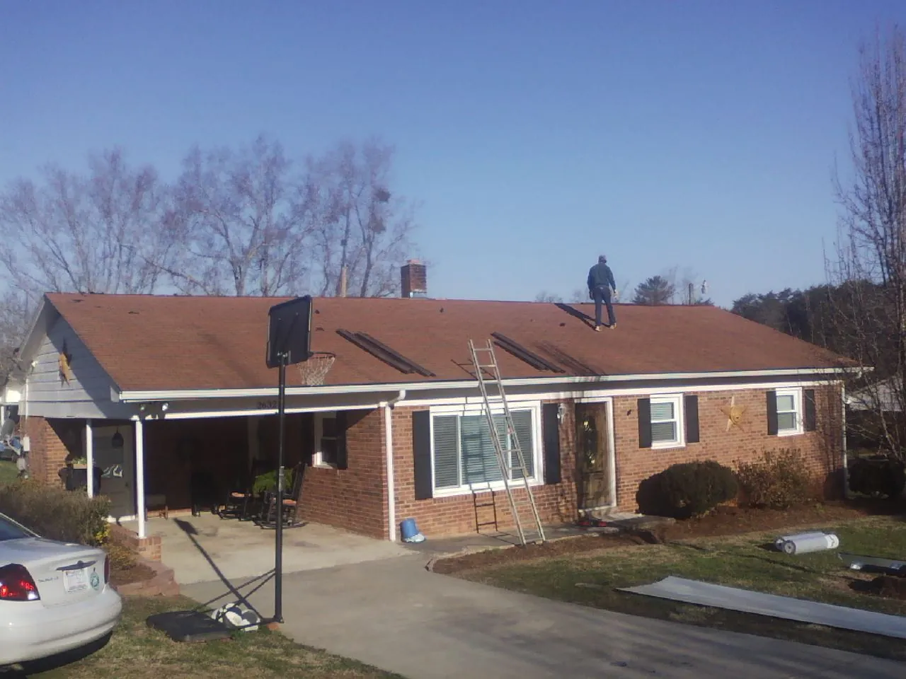 Roofer stripping a shingle roof on a brick ranch before metal panels in Canaan