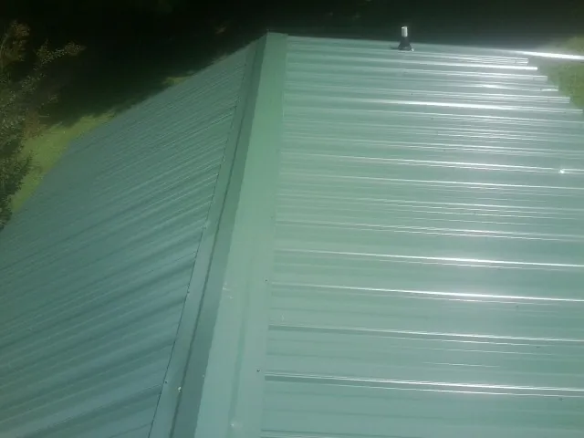 New green metal panels meeting at the ridge of a roof — Flat Roof Repair work by our crew in Canaan