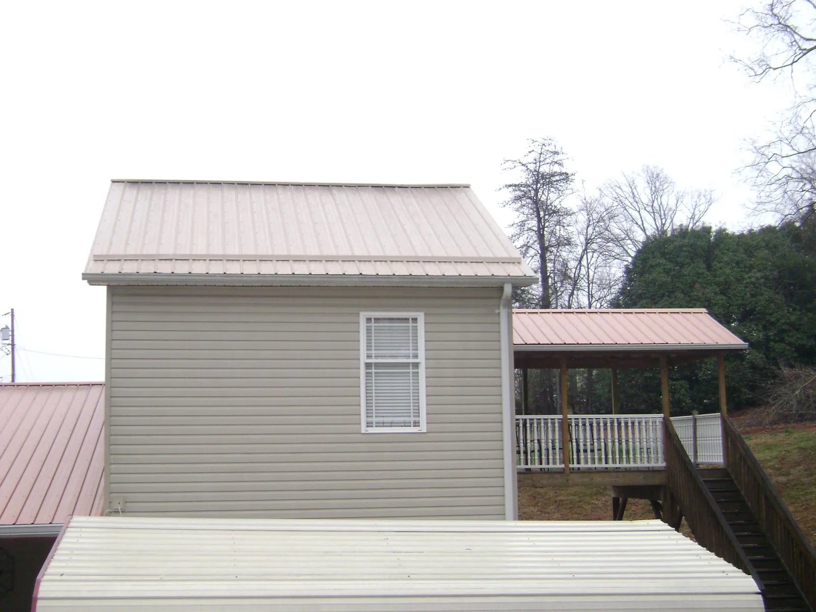 Tan metal roofs on a two story addition and attached porch, from a Roof Replacement job in Canaan